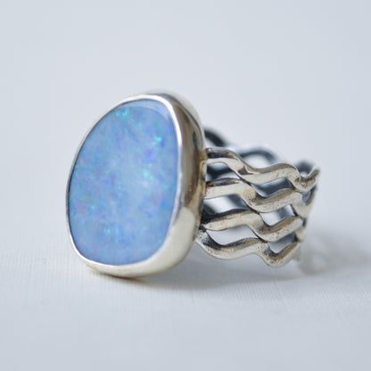 A silver ring featuring a large, irregularly shaped light blue opal gemstone in a polished bezel setting, with a wide, wavy openwork silver band.