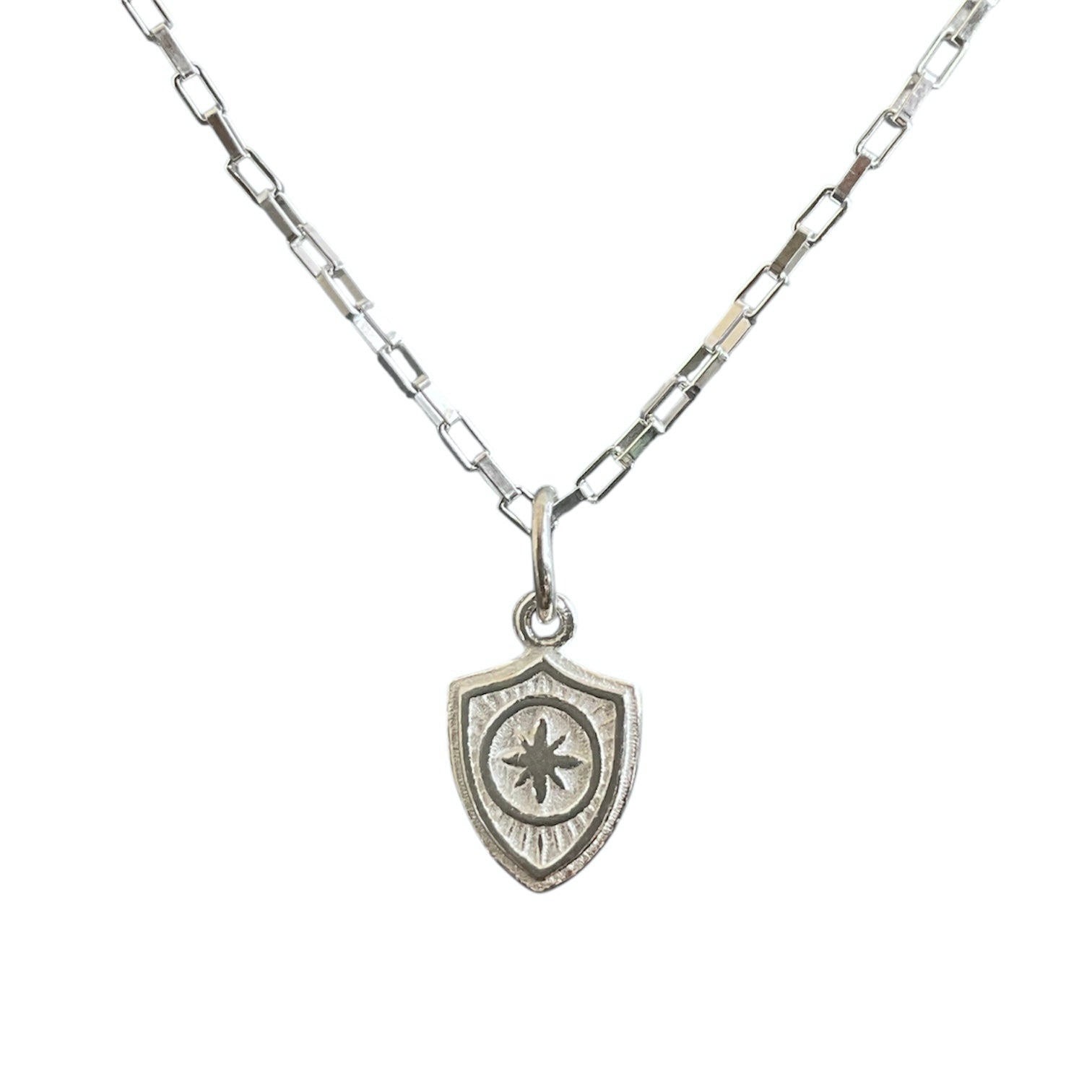 Sterling silver shield charm hanging on a baby paper clip chain.
