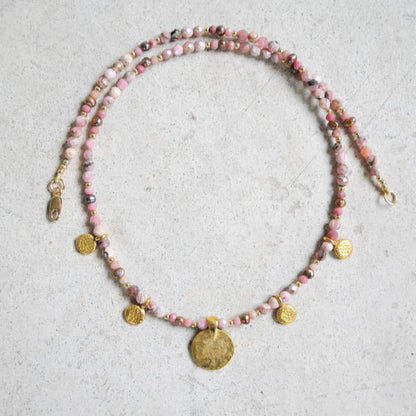 Rhodochrosite beaded necklace with gold coins on a textured surface