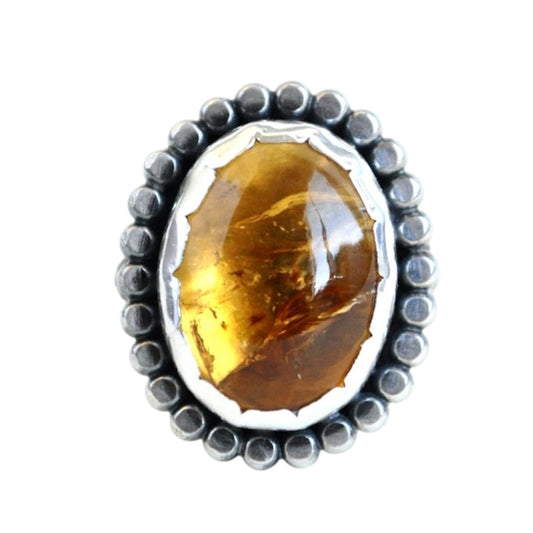 A citrine gemstone ring with a sterling silver band and a beaded border around the stone, which is set in a scalloped bezel.