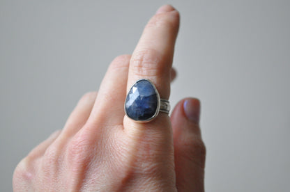 Hand wearing a ring with a blue stone on a neutral background