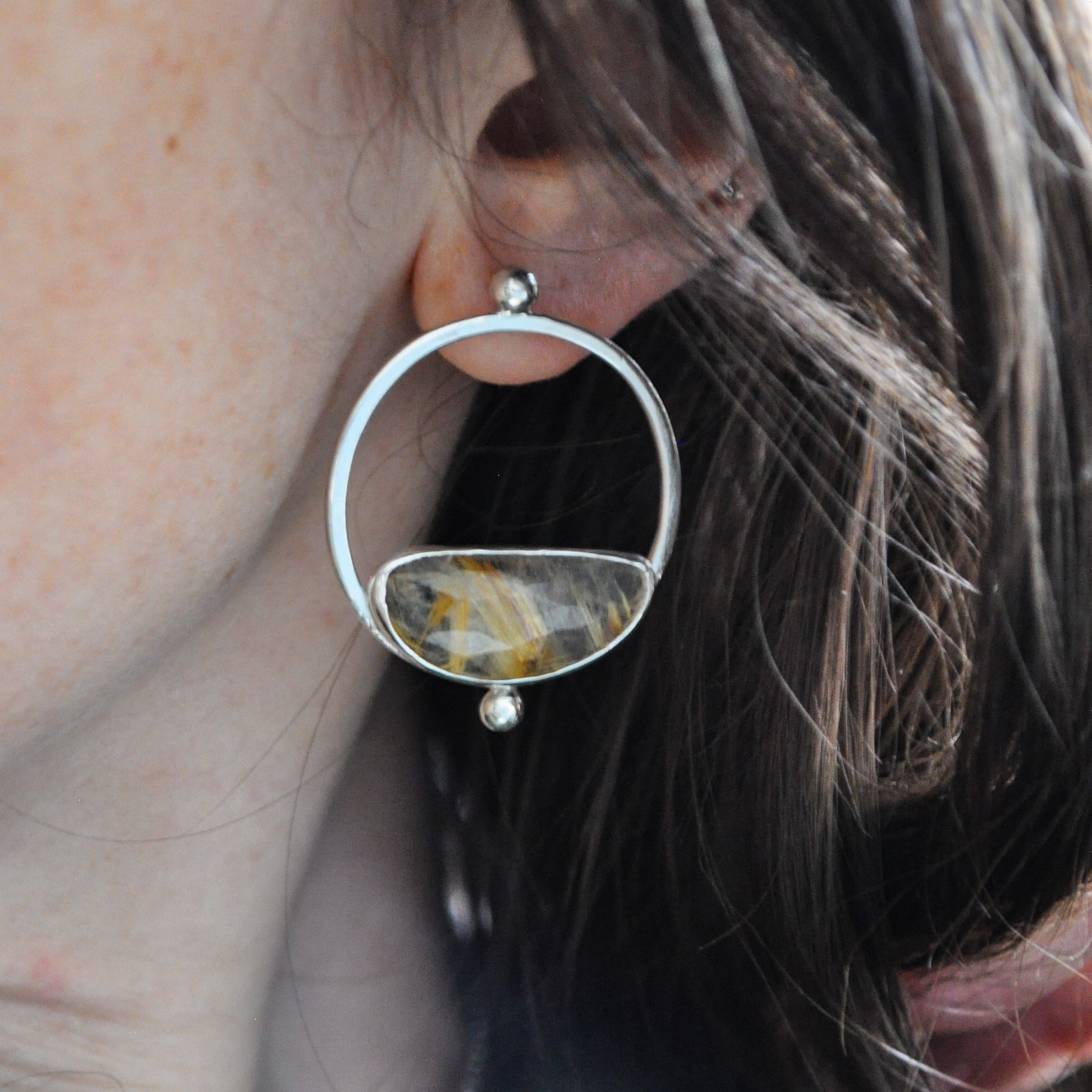 Close-up of a silver earring with a gemstone worn by a person.