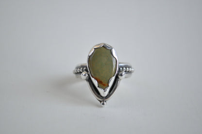 A sage green turquoise set in sterling silver with a scalloped bezel and a beaded band.