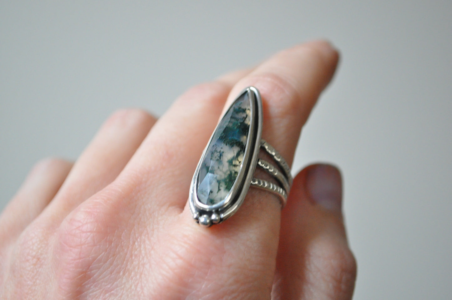Silver ring with a stone on a finger against a neutral background