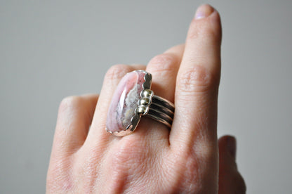 Hand wearing a silver ring with a pink stone on a neutral background