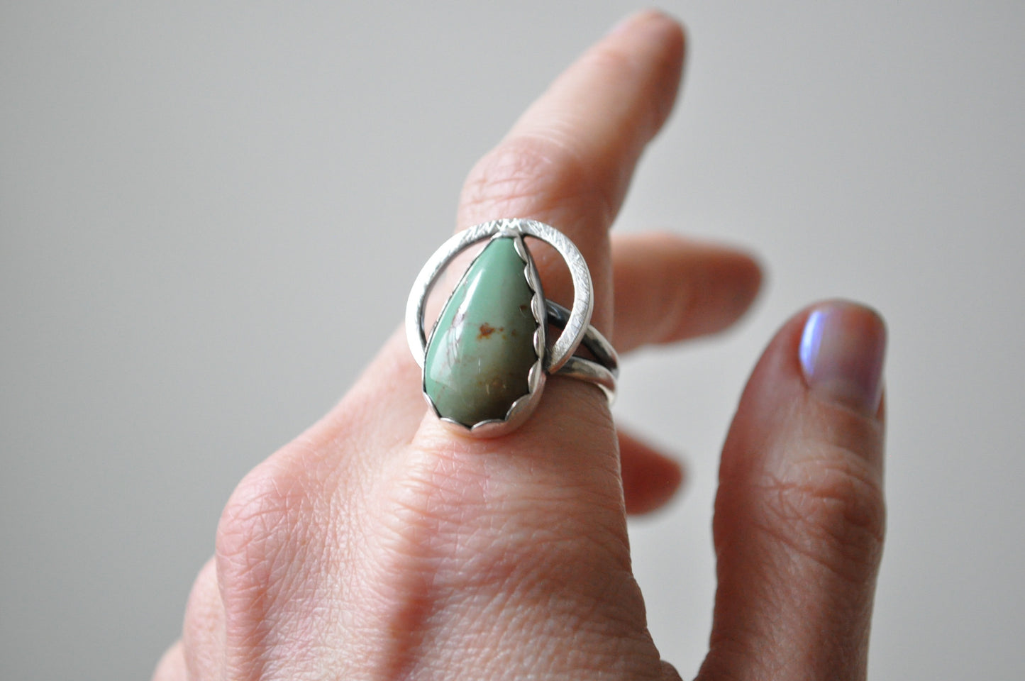 Hand wearing a silver ring with a green stone on a neutral background